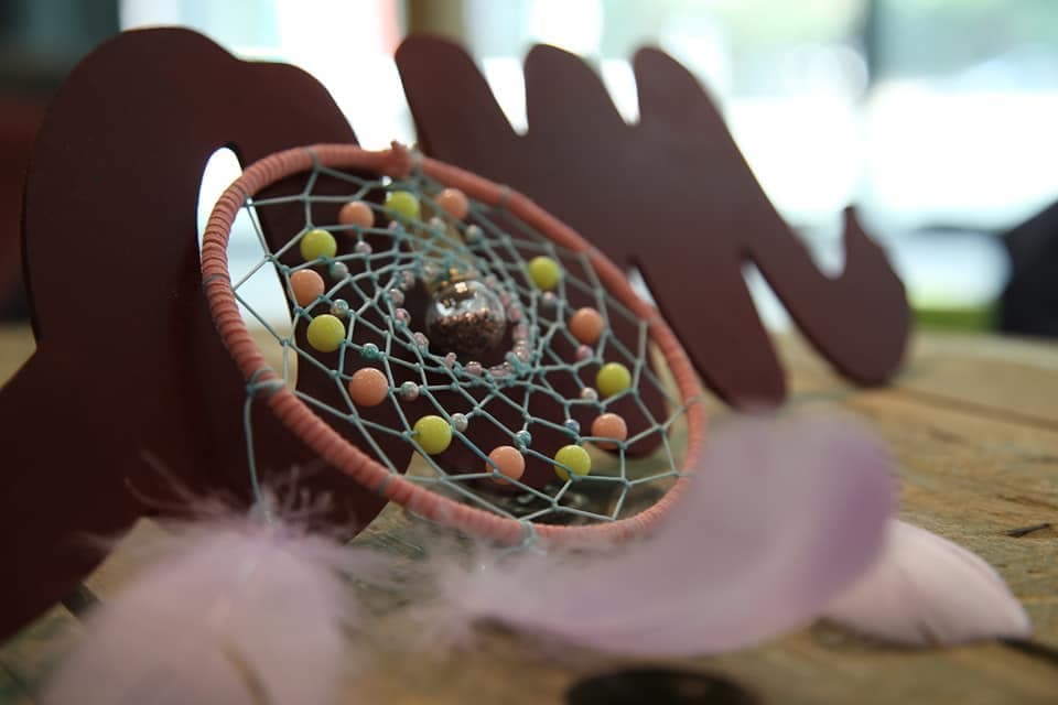 Small dreamcatcher with colorful beads and purple feathers resting against a dark brown wooden cutout.