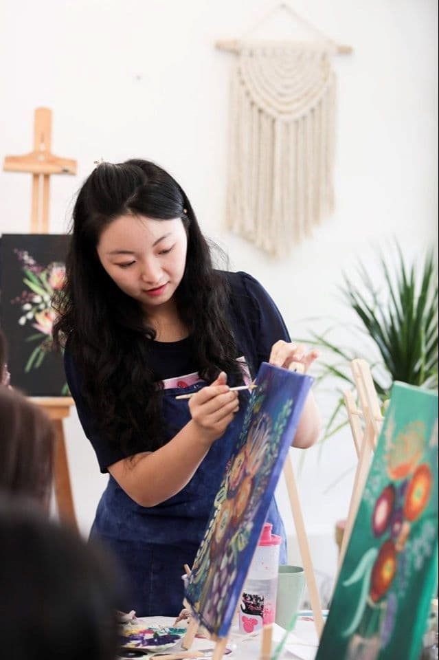 Focused young woman painting a colorful floral design on a canvas in an art studio.