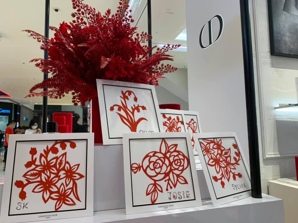 Framed red paper-cut floral art with names displayed at a Christian Dior boutique counter.