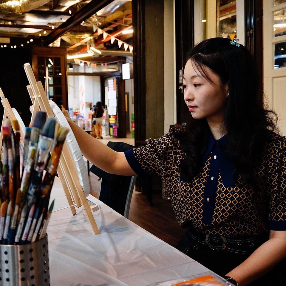 Young woman in a patterned shirt painting on a canvas in an art studio.