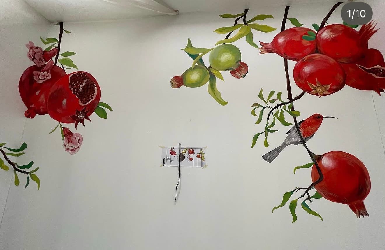 Wall mural featuring ripe red pomegranates, green fruit, blossoms, and a bird on branches.