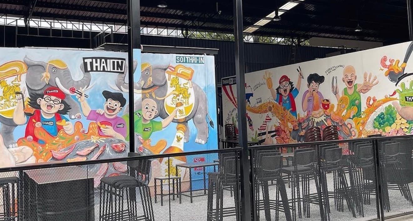 Vibrant cartoon murals of elephants and people decorate a modern outdoor restaurant with black seating.