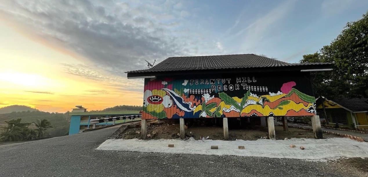 Vibrant abstract mural on a hillside building at Jerantut Hill Resort during a golden sunset.