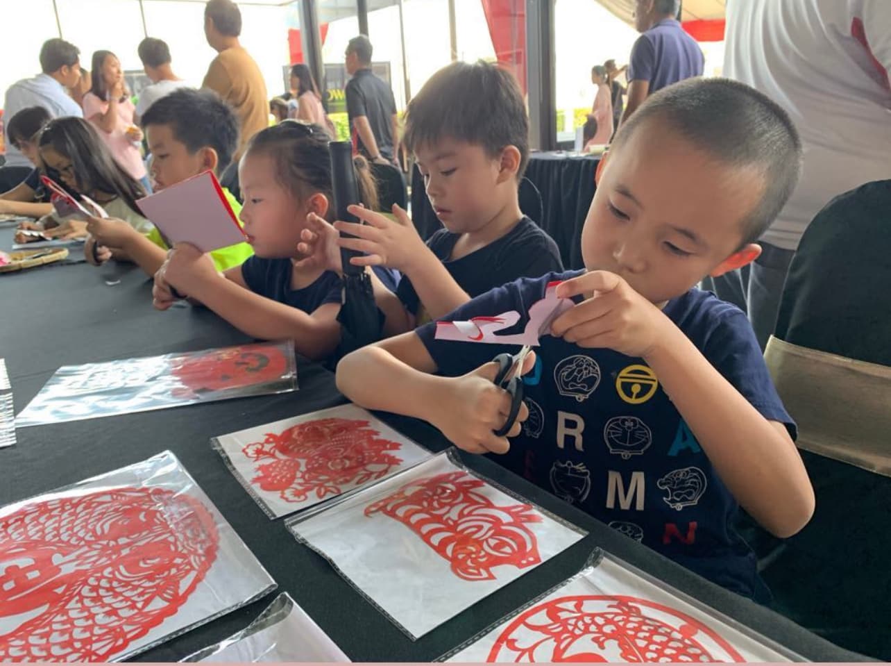 Children at a table carefully cutting out traditional red Chinese paper designs with scissors.