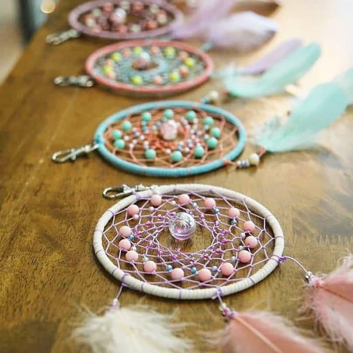 Colorful dreamcatcher keychains with intricate beadwork and soft feathers resting on a wooden table.