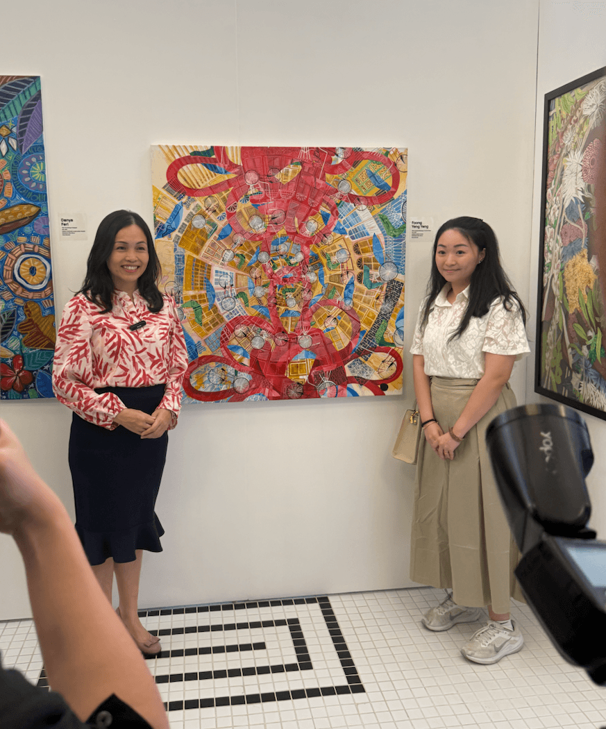 Two women stand beside a vibrant abstract painting displayed in a bright art gallery.