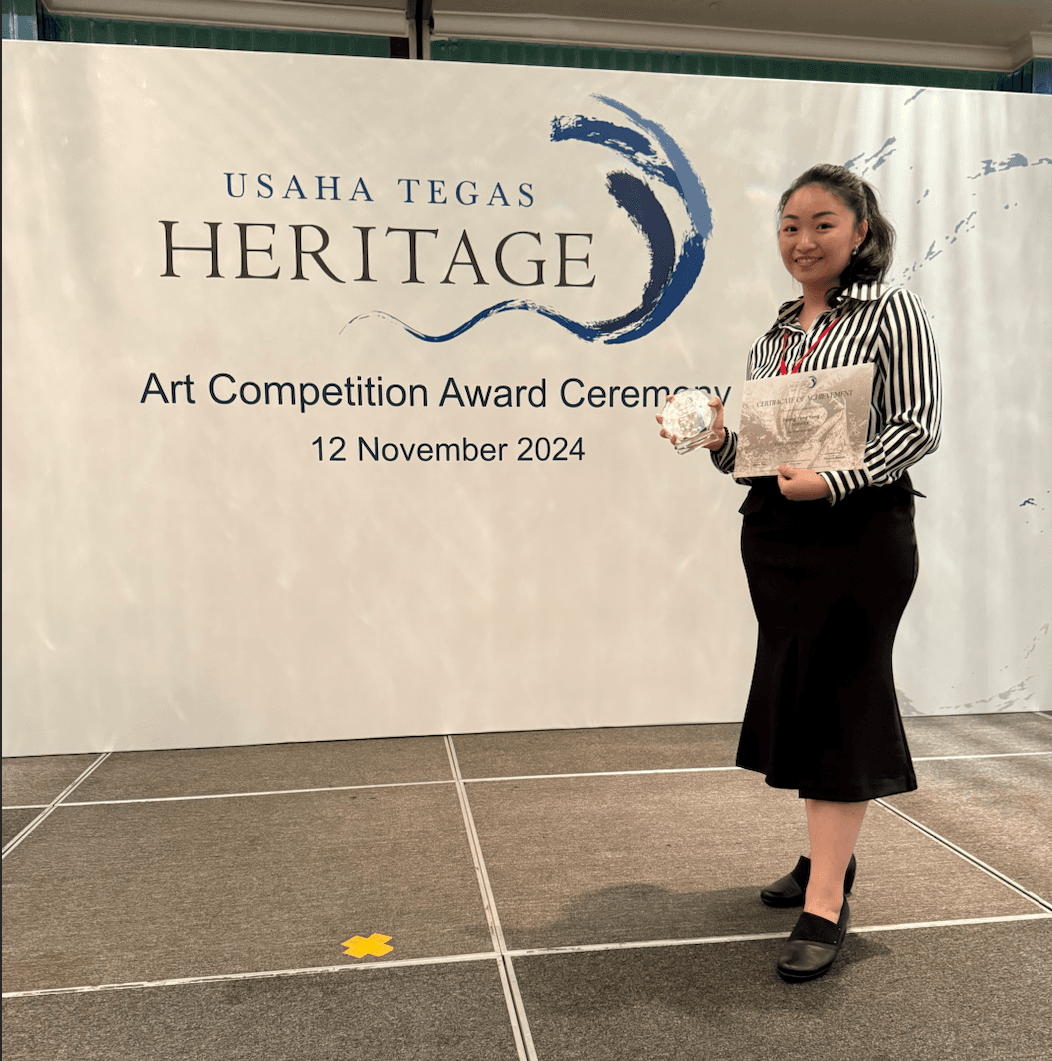 Woman holding a certificate and trophy at the Usaha Tegas Heritage Art Competition ceremony.